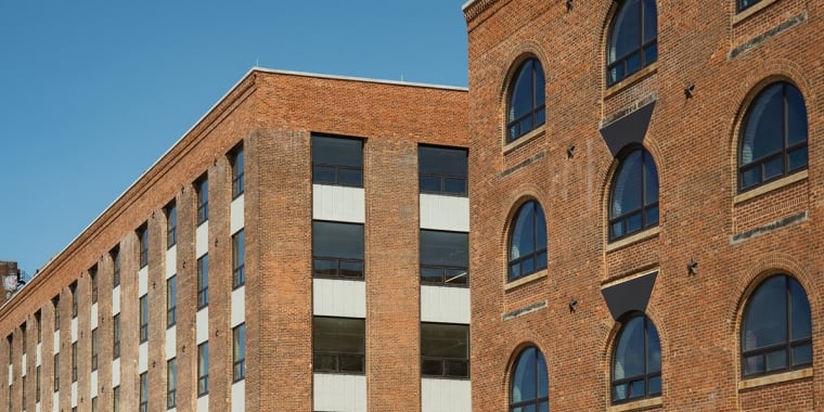 Two brick buildings with arched and rectangular windows against a clear blue sky.