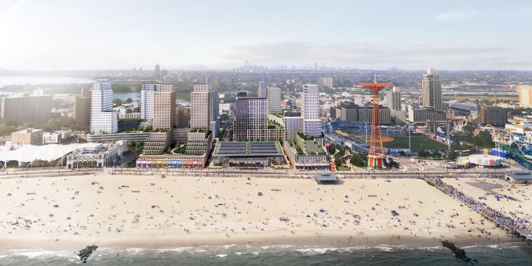 Aerial view of a beach with people, adjacent buildings, and a ferris wheel-like structure in an urban setting.