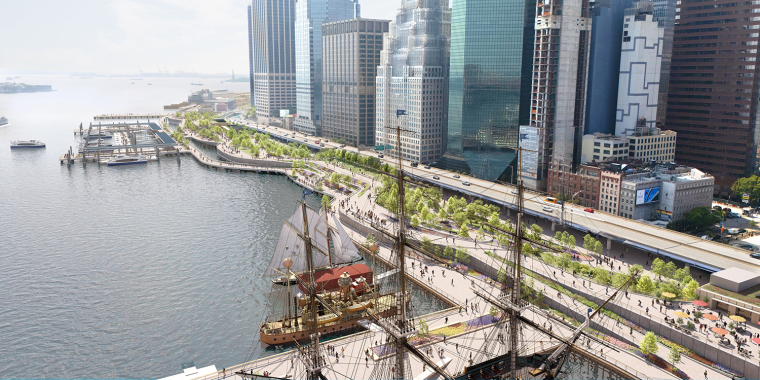 Aerial view of a waterfront cityscape with tall modern skyscrapers, a tree-lined promenade, docked historic sailing ships, and people walking along the water’s edge.