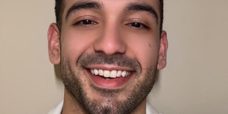 Kerem Asa with short dark hair and facial hair smiles at the camera, wearing a white collared shirt against a plain beige background.