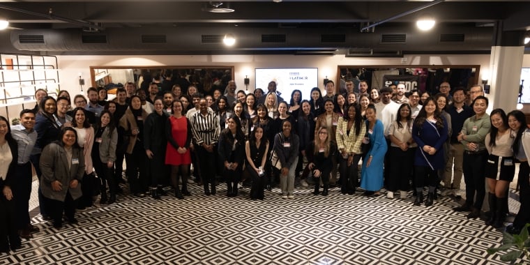 Members of the large, diverse 2025 Founder Fellowship cohort pose and smile for a group photo in a well-lit indoor space with patterned flooring.