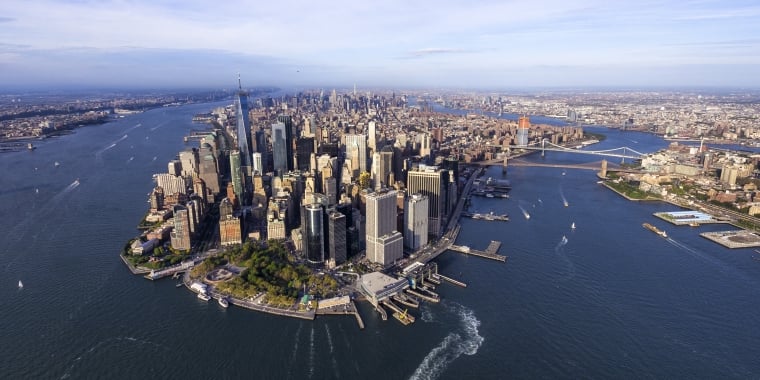 Aerial view of Lower Manhattan, New York City, showing skyscrapers, waterfront parks, and surrounding rivers with boats. The Brooklyn and Manhattan bridges are visible in the background. Photo by Eloi Omella/Getty Images.