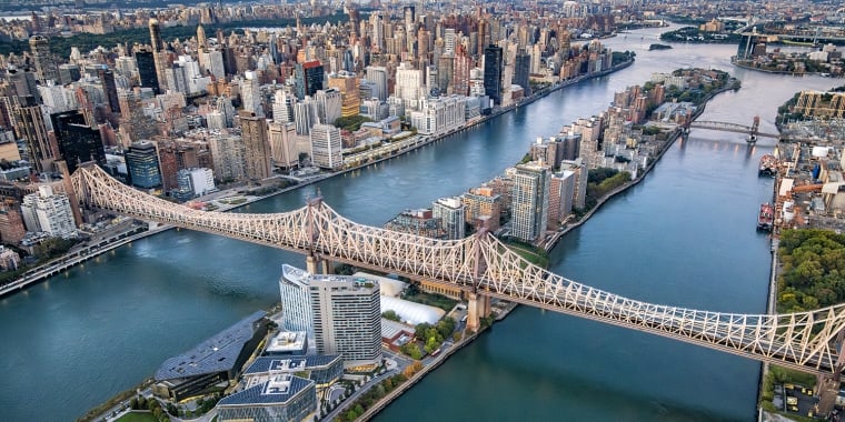 Aerial view of Roosevelt Island and the Ed Koch Queensboro Bridge spanning the East River, connecting Manhattan and Queens in New York City, with tall buildings and lush green spaces along the waterfront.