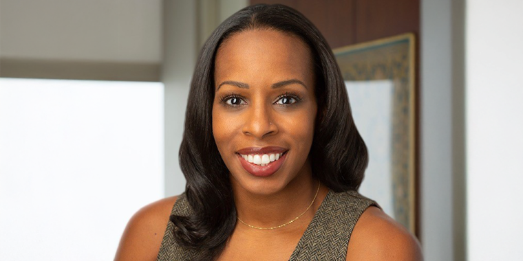 Headshot of Margaret Anadu shows a woman with long, dark hair and a nose piercing smiles at the camera. She is wearing a sleeveless brown top and a thin gold necklace, standing in an indoor setting with neutral-toned walls.