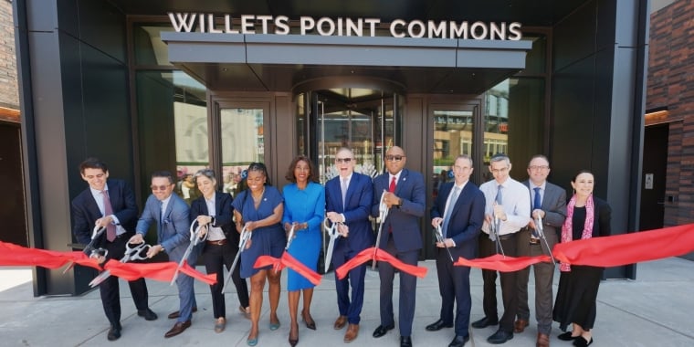 QDG team stands in front of Willets Point Commons, cutting a large red ribbon with oversized scissors during a ribbon-cutting ceremony. Image courtesy of QDG.