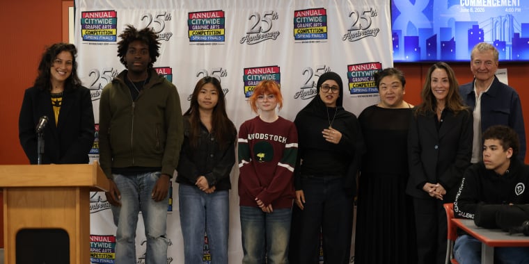 A group of nine people, including teens and adults, pose in front of a step-and-repeat banner for the “Annual Citywide Graphic Arts Competition Finals.” A podium is at the left.