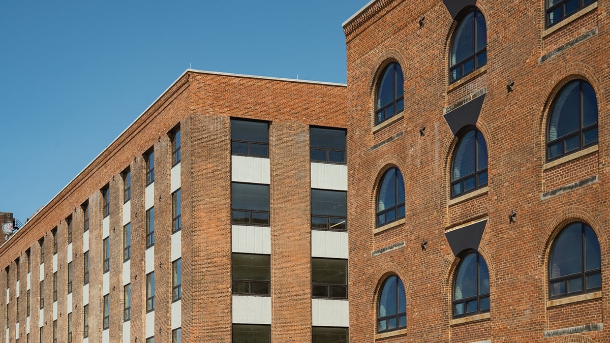 Corner view of MADE Bush Terminal. Two brick buildings with arched and rectangular windows against a clear blue sky.