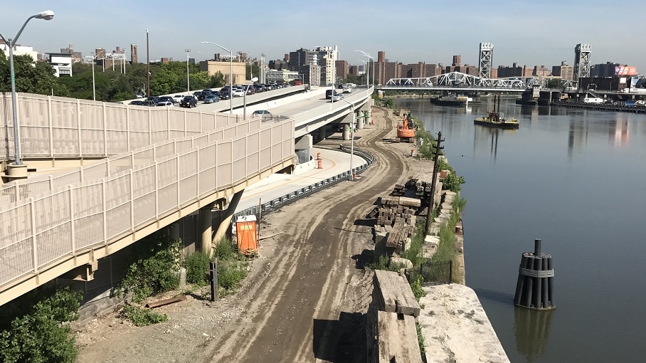 The Third Avenue bridge spans the Harlem River, with several cars traveling across the Harlem River Drive, showcasing a busy transportation route and the soon to be park below.