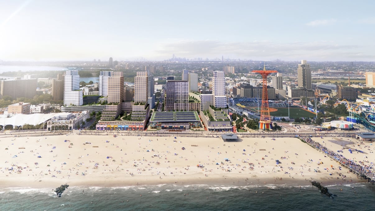 Aerial view of a beach with people, adjacent buildings, and a ferris wheel-like structure in an urban setting.