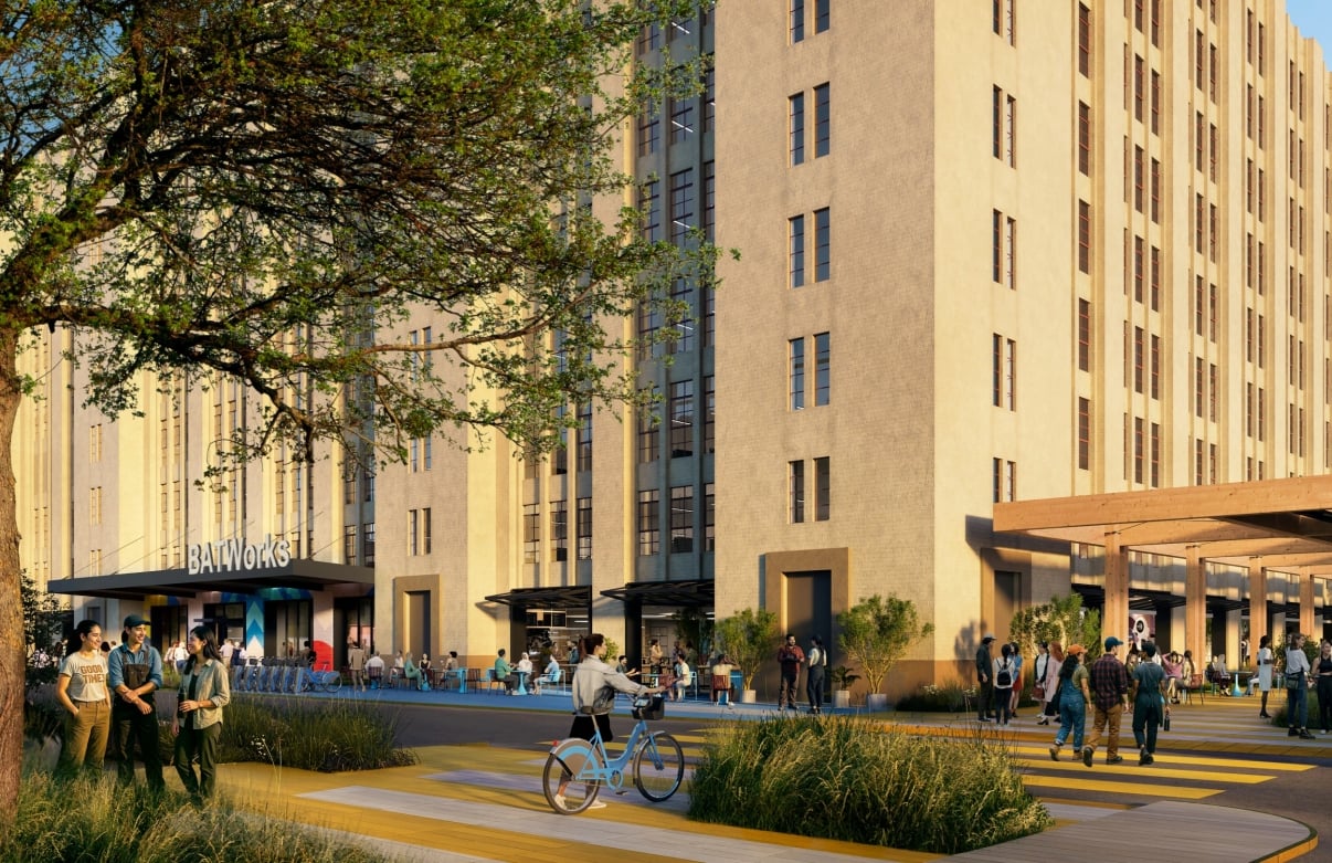 Lively outdoor plaza with people walking, cycling, and gathering near BATWorks, a tall beige building with large windows. There are trees, plants, and a shaded seating area, with a sign reading BATWorks visible in the background. Lively outdoor plaza with people walking, cycling, and gathering near BATWorks, a tall beige building with large windows. There are trees, plants, and a shaded seating area, with a sign reading BATWorks visible in the background.