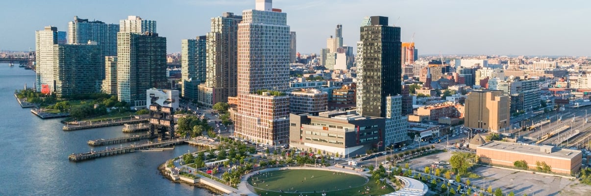 Aerial view of Hunter's Point South in Long Island City, Queens. The park features a large, circular green space surrounded by trees, a ferry terminal with a boat docked, and the East River with high-rise buildings lining the waterfront. Photo by Jonnu Singleton/SWA Group. Aerial view of Hunter's Point South in Long Island City, Queens. The park features a large, circular green space surrounded by trees, a ferry terminal with a boat docked, and the East River with high-rise buildings lining the waterfront. Photo by Jonnu Singleton/SWA Group.